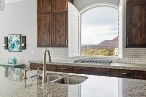 Kitchen featuring dark wood finish cabinets, light stone counters, a mountain view, stainless steel gas stovetop, and decorative backsplash