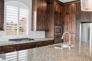 Kitchen with stainless steel appliances, light stone countertops, decorative backsplash, and dark wood finish cabinets