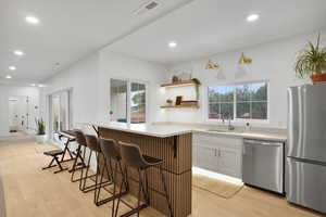down stairs Kitchenette featuring stainless steel appliances, light countertops, light wood finished floors, open shelves, and white cabinets