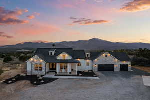Modern farmhouse featuring stone siding, covered porch, gravel driveway, and a mountain view