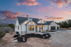Modern inspired farmhouse featuring stone siding, covered porch, driveway, and a chimney
