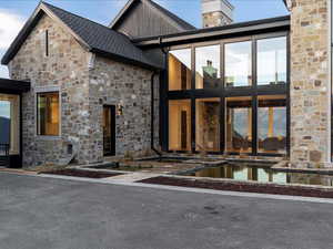 View of exterior entry featuring stone siding, a chimney, an outdoor pool, and a patio area