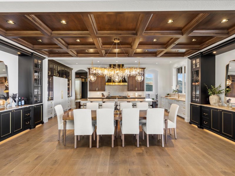 Kitchen with arched walkways, a large island with sink, coffered ceiling, glass fronted cabinets, and decorative light fixtures
