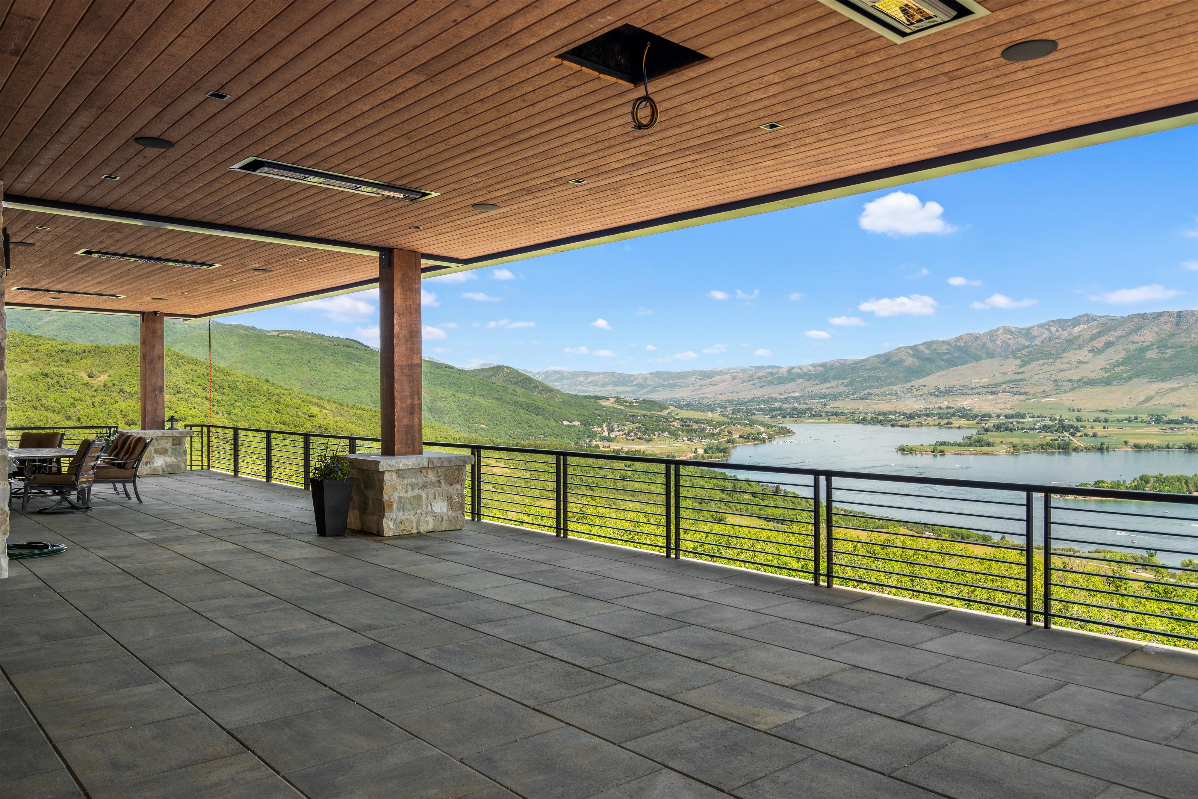 Expansive covered outdoor patio featuring large format pavers, a wood-finish ceiling with recessed lighting and mounted heaters, and stone-clad columns