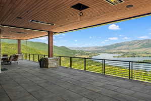 Expansive covered outdoor patio featuring large format pavers, a wood-finish ceiling with recessed lighting and mounted heaters, and stone-clad columns