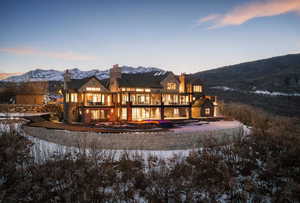 Snow covered back of property featuring a chimney, a mountain view, and a patio