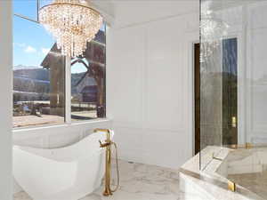 Full bath with a decorative wall, a chandelier, a mountain view, marble look tile flooring, and a soaking tub