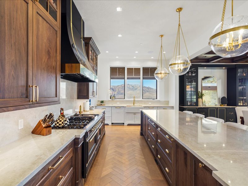 Dual tone kitchen with light stone countertops, glass insert cabinets, double oven range, pendant lighting, and two tone cabinetry