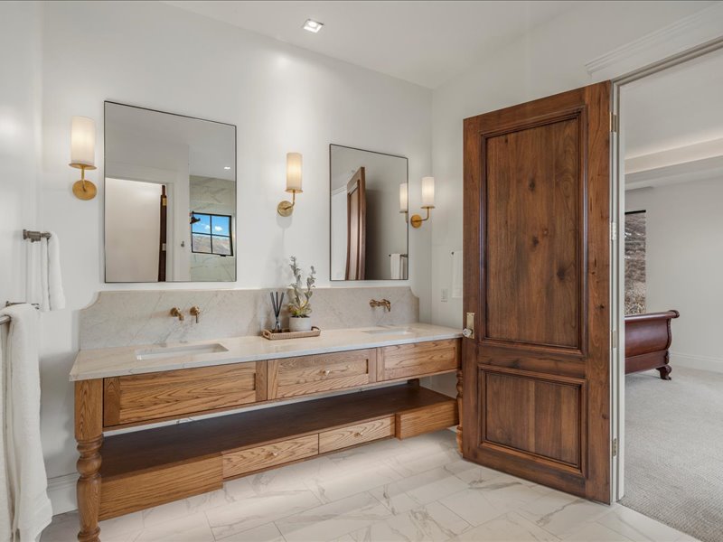 Bathroom featuring double vanity, light marble finish flooring, and backsplash