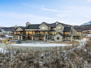 Snow covered house with stone siding, a mountain view, a chimney, and a balcony