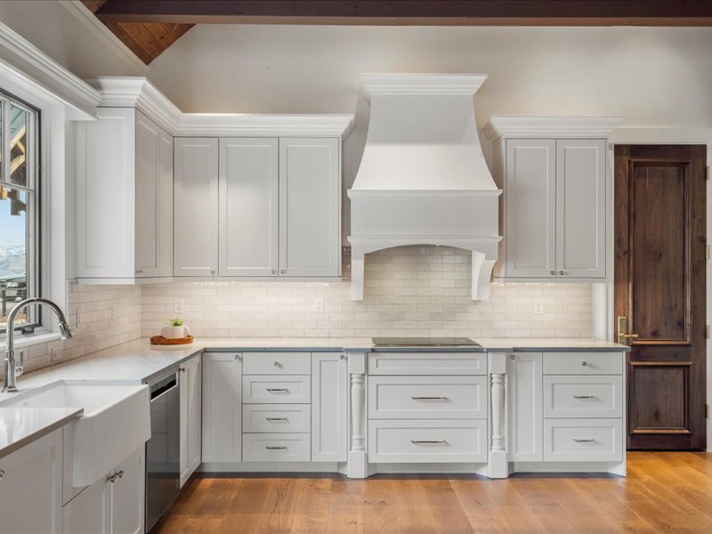 Kitchen with light stone counters, light wood-style floors, stainless steel dishwasher, white cabinets, and lofted ceiling with beams