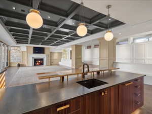 Kitchen with coffered ceiling, dark wood finished floors, modern cabinets, hanging light fixtures, and a lit fireplace