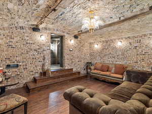 Living room with wood-type flooring, brick wall, suspended lighting, and a brick barrel ceiling