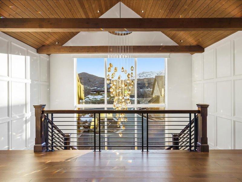 Corridor with an upstairs landing, a mountain view, hanging lights, a wooden ceiling with exposed beams, and a decorative wall