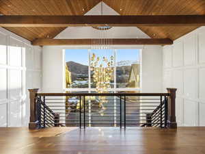 Corridor with an upstairs landing, a mountain view, hanging lights, a wooden ceiling with exposed beams, and a decorative wall