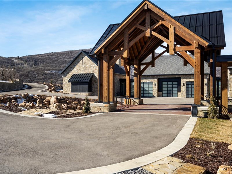 View of front facade with asphalt driveway, a standing seam roof, a patio, and stone siding