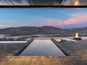 Pool at dusk with a fire pit, a mountain view, a patio, and an infinity pool