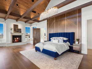 Bedroom with wood finished floors, a warm lit fireplace, a high wood beamed ceiling, and recessed lighting