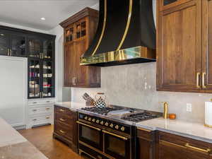 Dual tone kitchen with glass insert cabinets, range with two ovens, two tone cabinets, light stone counters, and dark wood-style floors