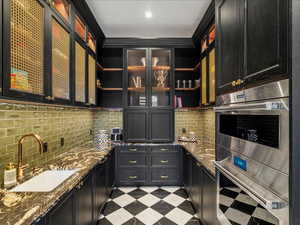 Bar area with open shelves, dark cabinets, and double oven