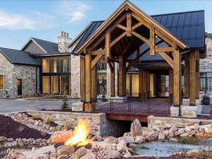 Back of house with an outdoor fire pit, a chimney, stone siding, and a patio