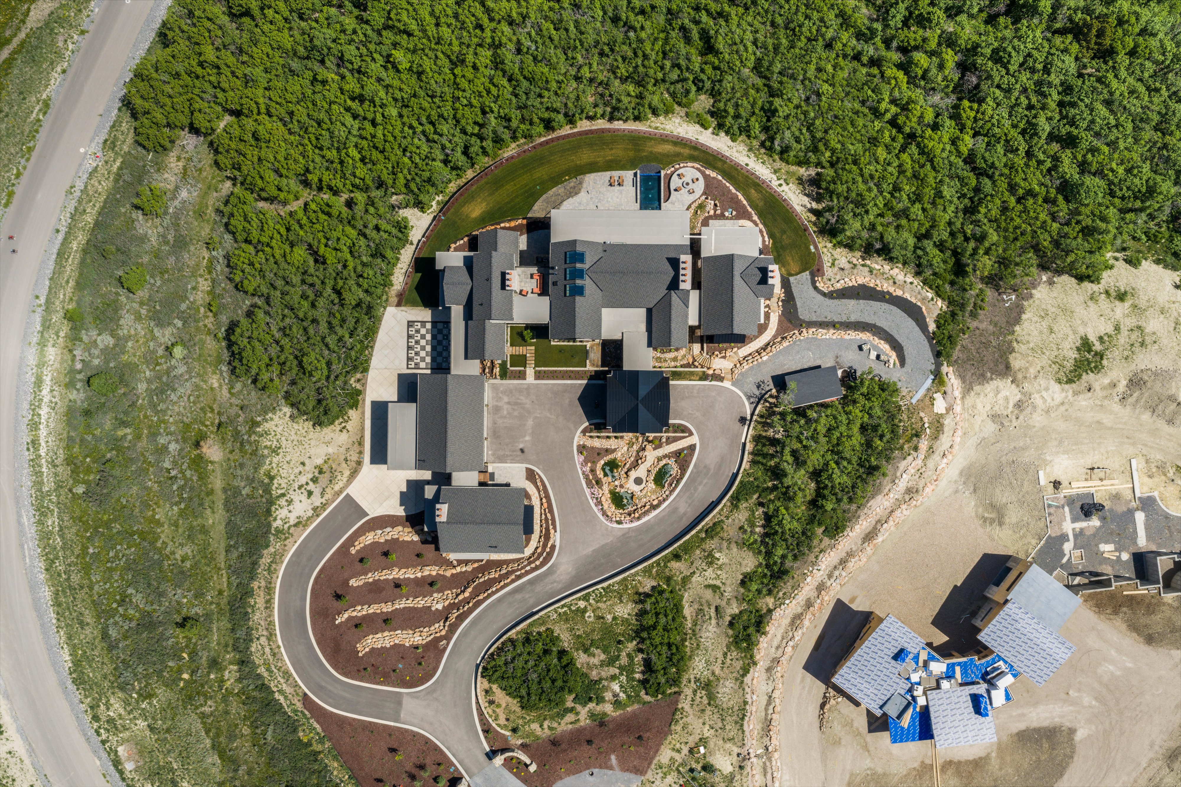 Expansive property featuring a multi-structure residence with dark-toned roofing, a swimming pool, and extensive paved driveways