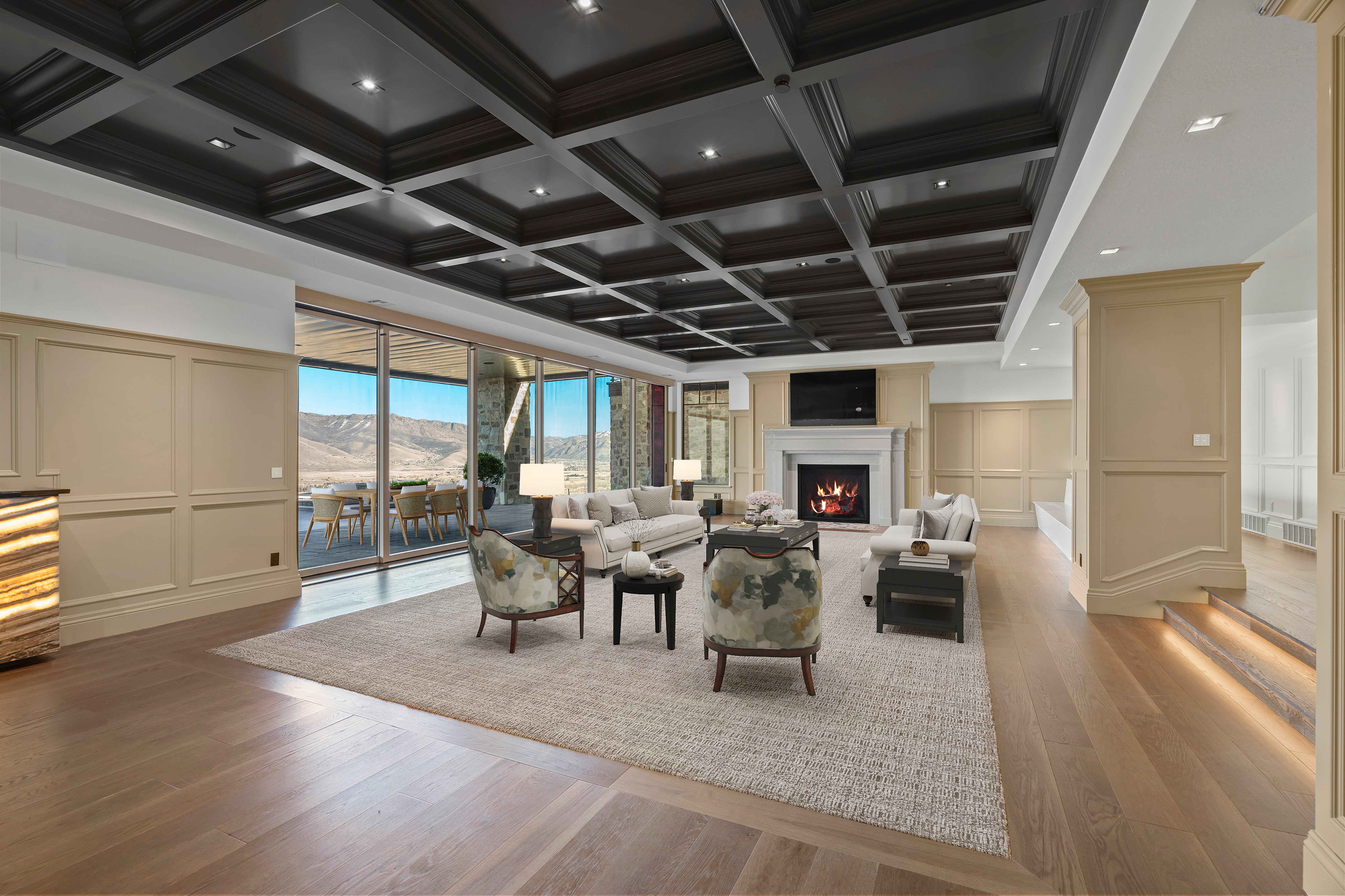 Living room with a decorative wall, coffered ceiling, light wood-style flooring, a warm lit fireplace, and recessed lighting