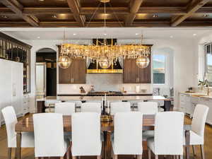 Two tone kitchen featuring coffered ceiling, dark wood-type flooring, light stone countertops, an island with sink, and two tone cabinetry