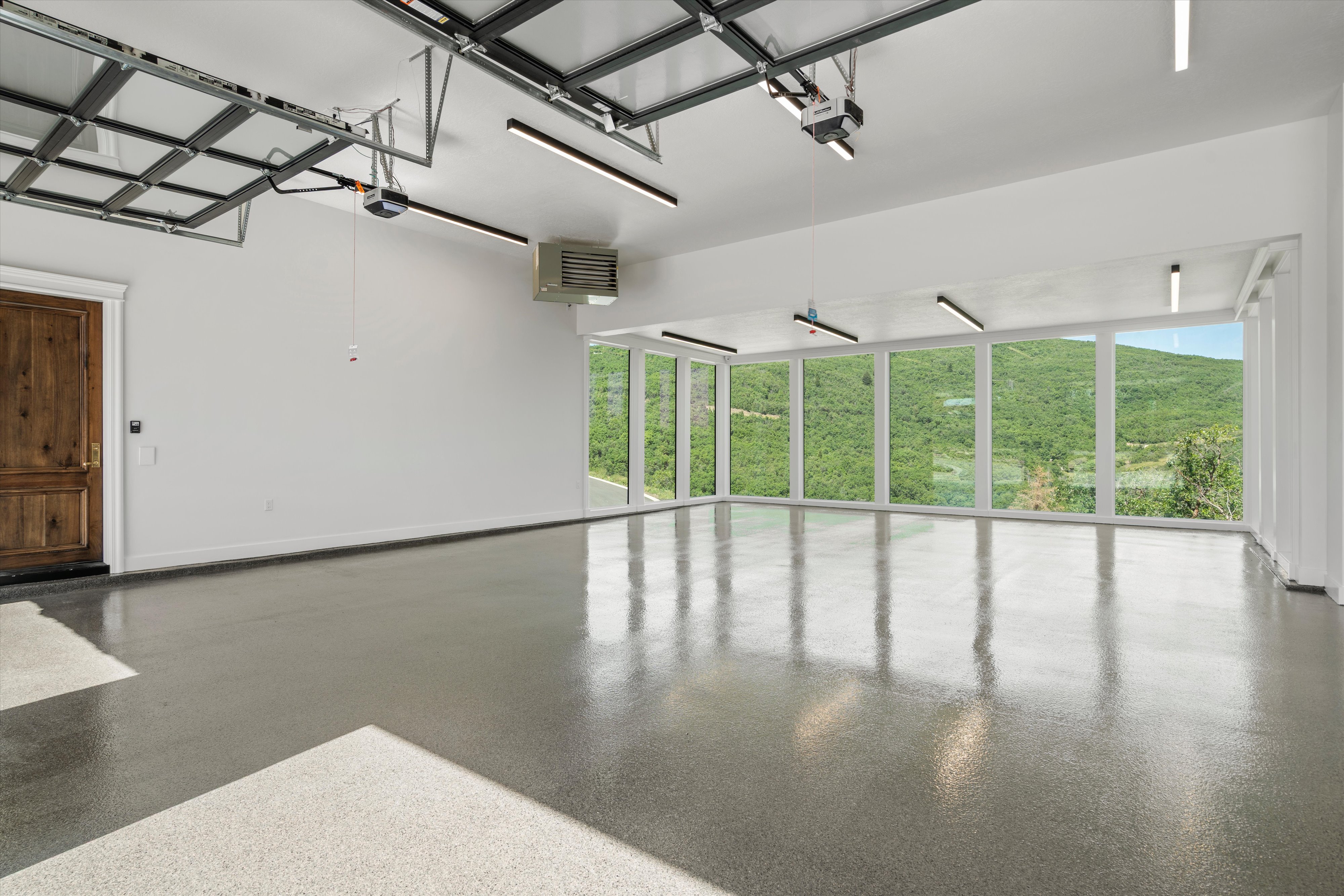 Expansive garage space featuring a polished epoxy floor, a richly textured wood door, and a wall of floor-to-ceiling windows