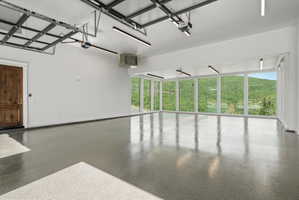 Expansive garage space featuring a polished epoxy floor, a richly textured wood door, and a wall of floor-to-ceiling windows