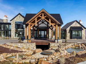 View of front of property with a standing seam roof, stone siding, a patio area, a small pond, and roof mounted solar panels