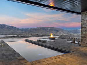 Patio terrace at dusk featuring an outdoor fire pit, a mountain view, and a patio area