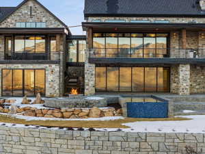 Back of house featuring a balcony, a patio area, stone siding, and roof with shingles