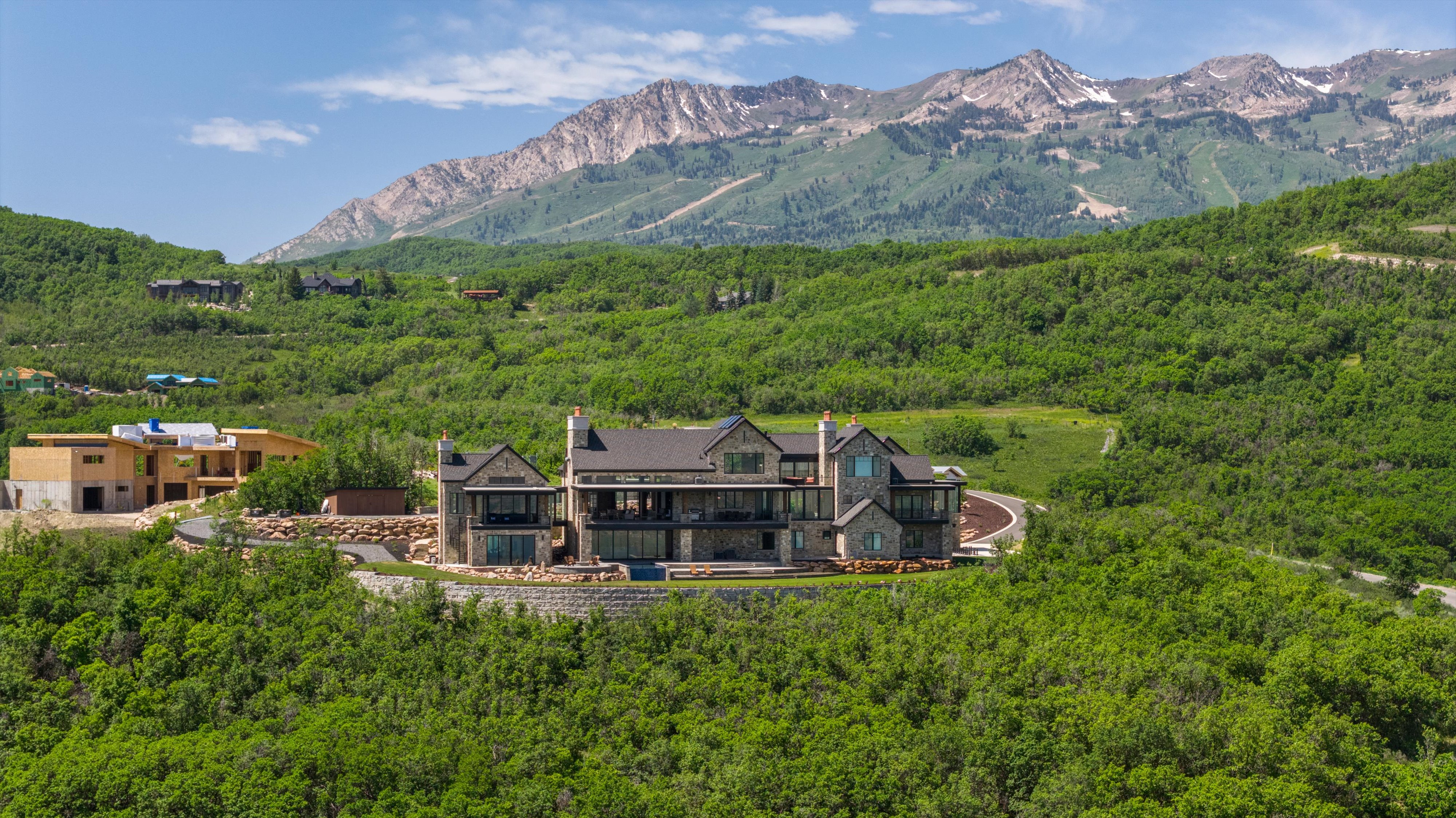 Expansive mountain estate featuring a stone and siding exterior, multiple levels of outdoor patio space, and a mountainous backdrop