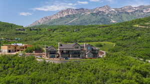 Expansive mountain estate featuring a stone and siding exterior, multiple levels of outdoor patio space, and a mountainous backdrop