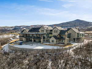 Back of property featuring a mountain view, a balcony, stone siding, a patio, and a chimney