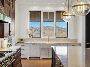Kitchen with dual tone cabinets, glass insert cabinets, light stone counters, stainless steel stove, and light wood-type flooring