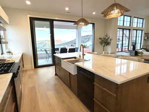 Kitchen with light wood-type flooring, black appliances, a mountain view, a kitchen island with sink, and hanging light fixtures