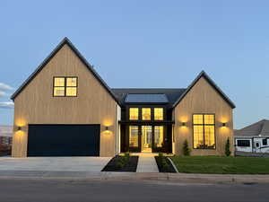 Modern inspired farmhouse featuring a standing seam roof, concrete driveway, roof mounted solar panels, a front yard, and a garage