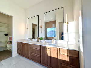 Bathroom featuring double vanity, a stall shower, a walk in closet, and light marble finish flooring