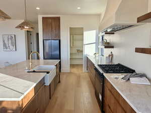 Kitchen with wood finish cabinets, range with gas stovetop, light wood-style flooring, and a large island with sink