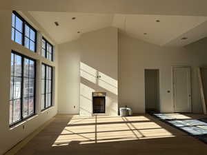 Unfurnished living room featuring wood finished floors, a high end fireplace, and vaulted ceiling