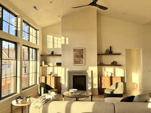 Living area featuring wood finished floors, a fireplace, a ceiling fan, and lofted ceiling