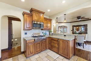 Kitchen with decorative light fixtures, arched walkways, wood finish cabinets, and a peninsula