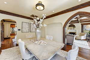 Dining room with arched walkways, dark wood-style floors, a fireplace, crown molding, and recessed lighting