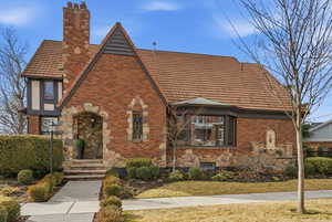 View of front of house featuring a chimney, brick siding, stone siding, and a tiled roof
