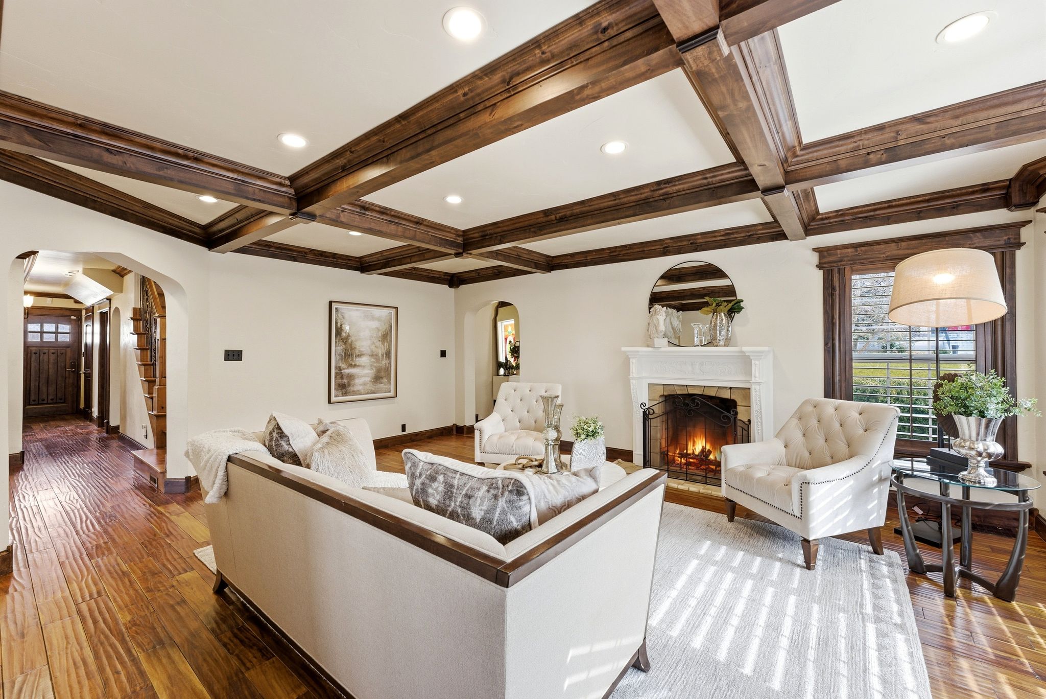 Living room with coffered ceiling, hardwood / wood-style floors, arched walkways, a lit fireplace, and recessed lighting