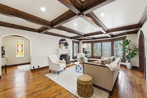 Living area featuring arched walkways, coffered ceiling, a fireplace with flush hearth, wood-type flooring, and recessed lighting