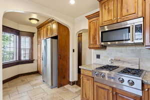 Kitchen with light stone countertops, wood finish cabinets, stainless steel appliances, and stone tile flooring