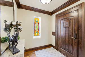 Foyer entrance with crown molding and dark wood-style floors
